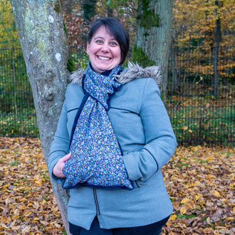 Femme souriante avec écharpe Baie rose à manchon, en extérieur, ready pour l'hiver.