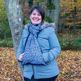 Femme souriante avec écharpe Baie rose à manchon, en extérieur, ready pour l'hiver.