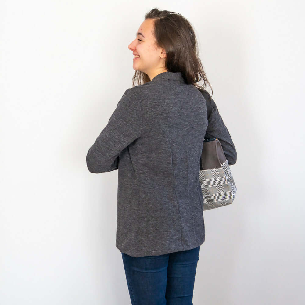 Femme portant un gilet Jasmin gris, vue de dos, avec un sac à main, parfait pour la mi-saison.