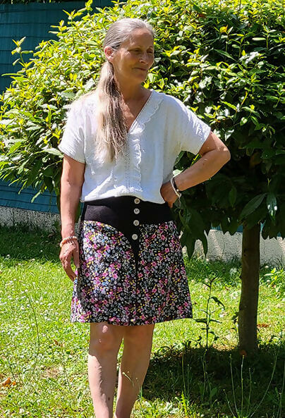 Femme portant une Jupe Améthyste fleurie avec un haut blanc, dans un jardin, patron de couture pdf à télécharger disponible.