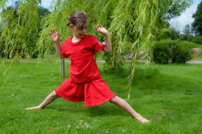 Jeune fille en jupe-short rouge à pois, jouant sous un arbre, idéale pour les activités d'été en toute liberté.