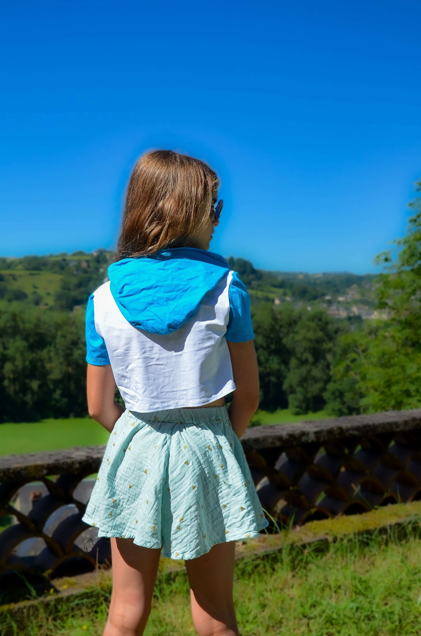 Girl wearing a blue and white outfit with a skirt, standing outdoors against a scenic background.