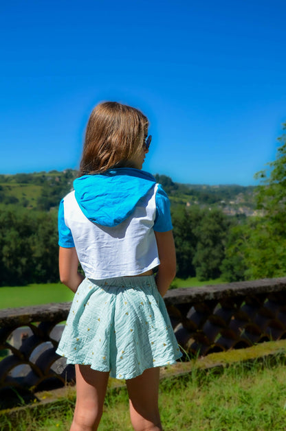 Girl wearing a blue and white outfit with a skirt, standing outdoors against a scenic background.