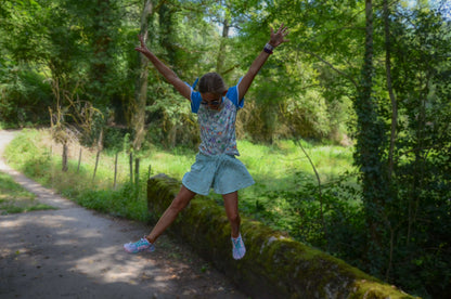 A girl joyfully jumping in a green landscape, wearing a stylish Jupe Culotte perfect for summer fun.