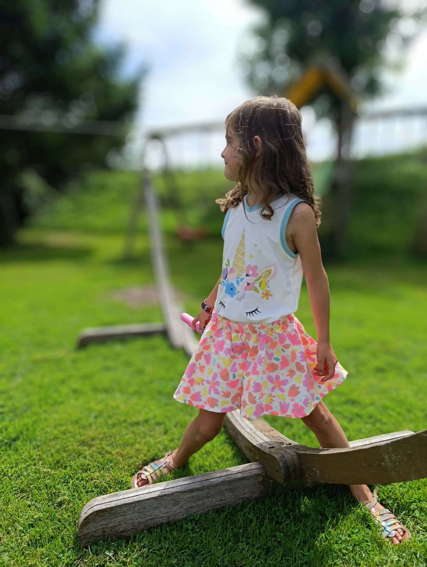 Petite fille en jupe culotte colorée s'amusant sur une balançoire dans un parc ensoleillé.