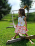 Petite fille en jupe culotte colorée s'amusant sur une balançoire dans un parc ensoleillé.