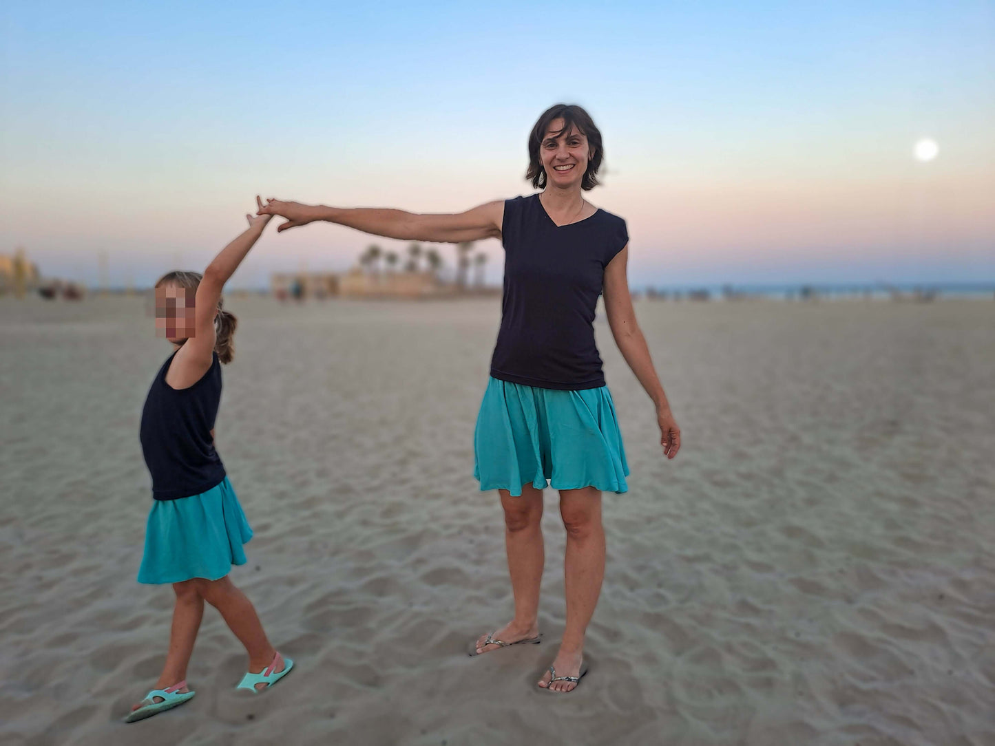 Mère et fille à la plage, vêtues de jupes courtes colorées, s'amusant ensemble au coucher du soleil.