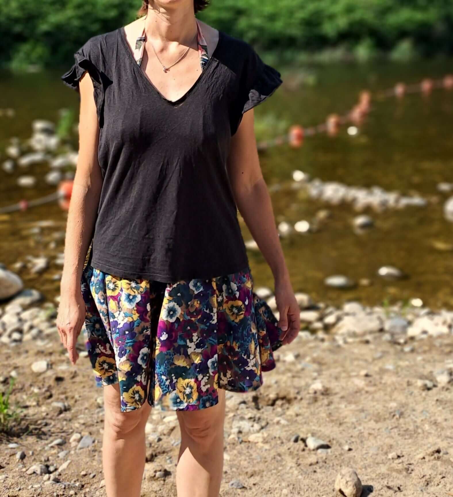 Femme portant un t-shirt noir et une jupe colorée près d'une rivière, idéale pour l'été.