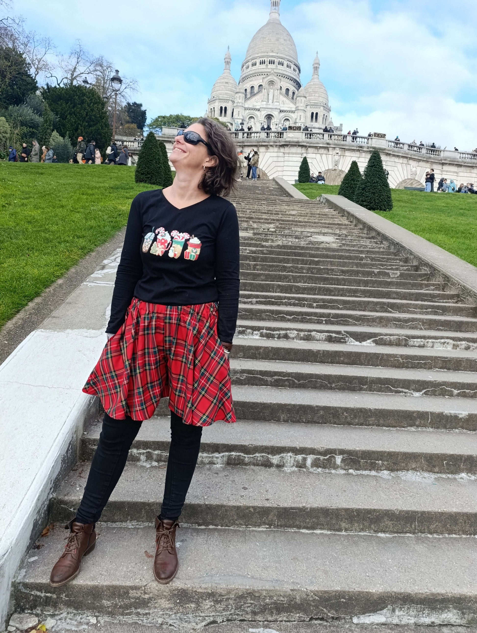Femme portant une jupe écossaise rouge et un top noir, posant sur les escaliers en face du Sacré-Cœur à Paris.