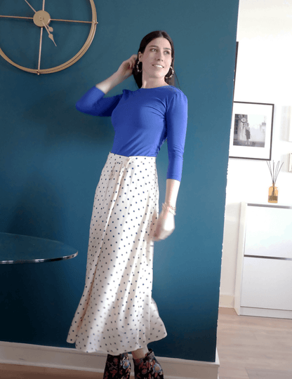 Femme portant une jupe Suzie à pois avec un haut bleu, dans un intérieur moderne et lumineux.