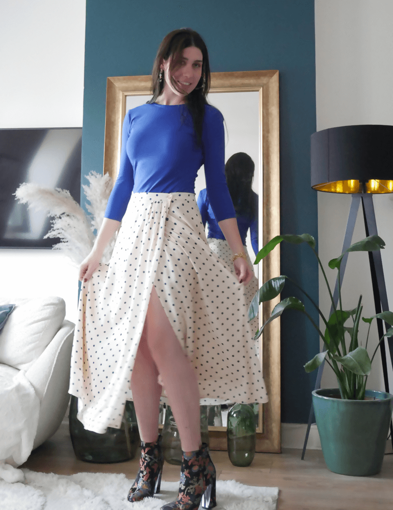 Jeune femme portant la jupe Suzie à pois, combinée avec un top bleu, dans un cadre moderne et chic.