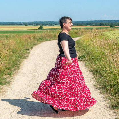 Femme portant la Jupe bohème Mirabelle rouge à motifs fleuris, dans une campagne, modèle de patron de couture pdf à télécharger.
