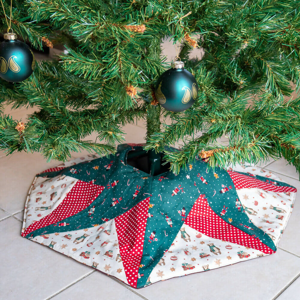 Jupe de sapin de Noël avec un motif étoilé, en tissu patchwork rouge et vert, embellissant le pied de l'arbre de Noël.