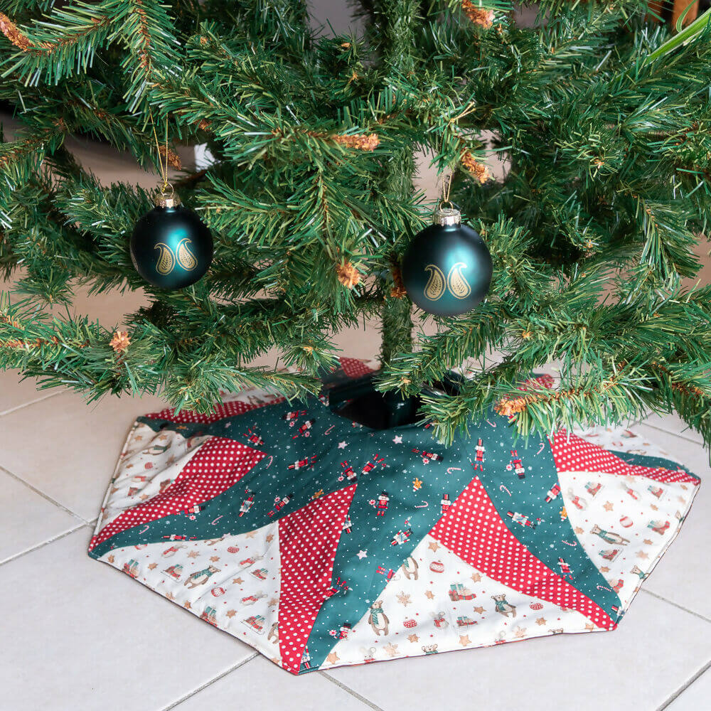 Jupe de sapin de Noël étoilée, décorée de motifs colorés, idéale pour camoufler le pied de l'arbre pendant les fêtes.