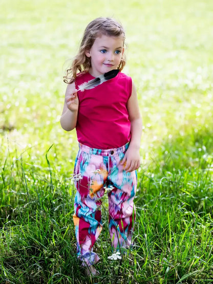 Enfant portant un pantalon coloré dans un parc, tenant une plume, en été.