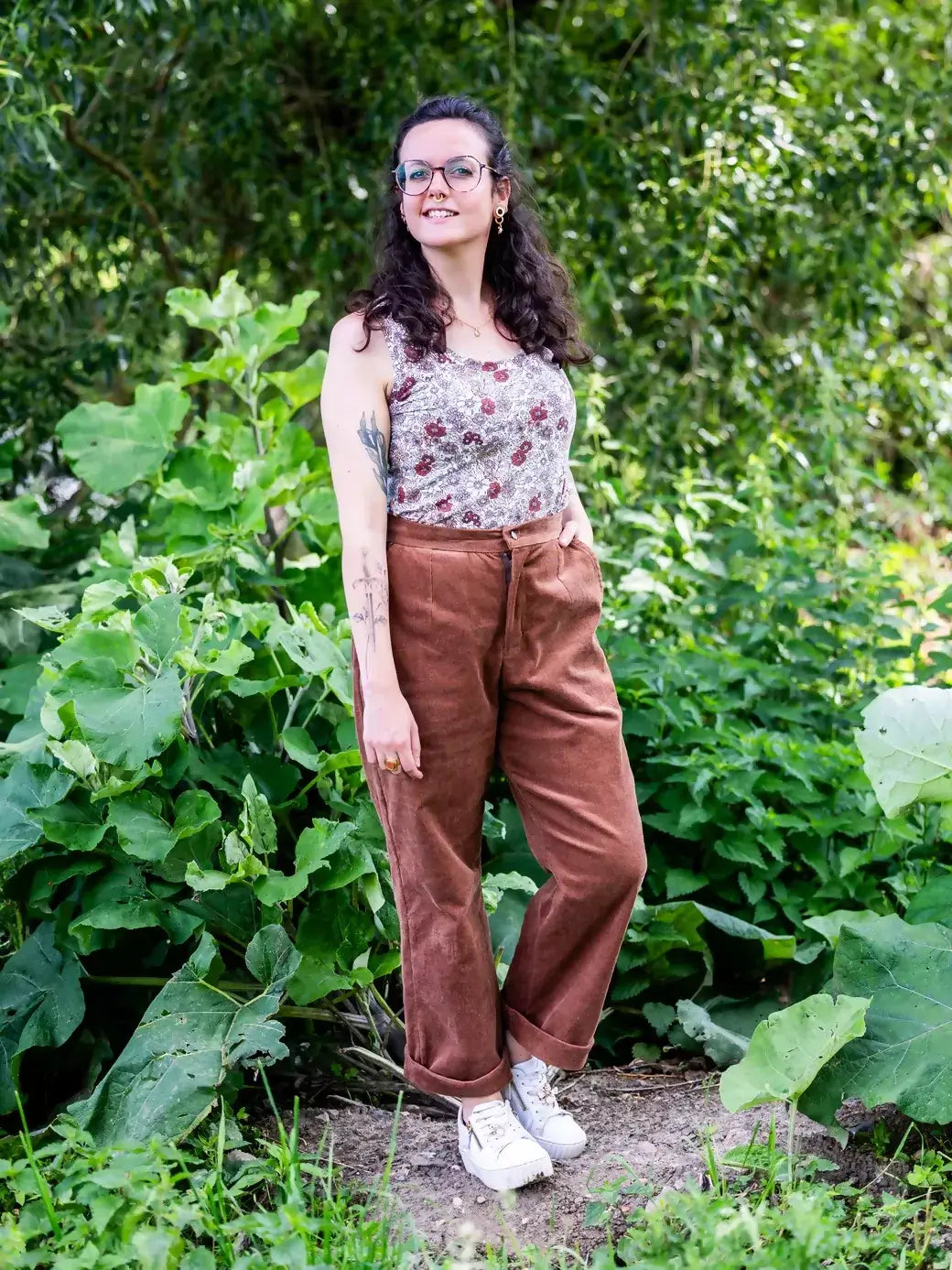 Femme portant KAKI - Le pantalon chino large, patron de couture PDF à télécharger, devant un fond de verdure.