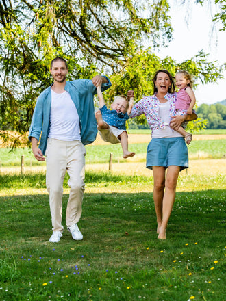 Famille souriante jouant dans le parc par une journée ensoleillée, les parents tenant les enfants par la main sous les arbres.
