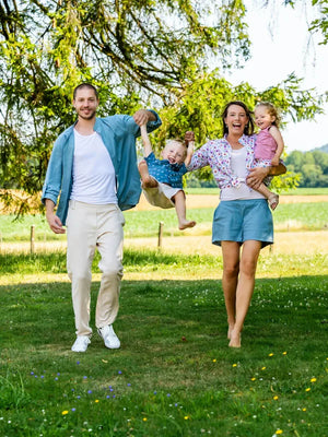 Famille souriante jouant dans le parc par une journée ensoleillée, les parents tenant les enfants par la main sous les arbres.