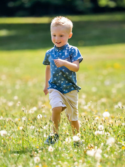 Enfant courant joyeusement dans un champ, portant une chemise bleue et un short beige.