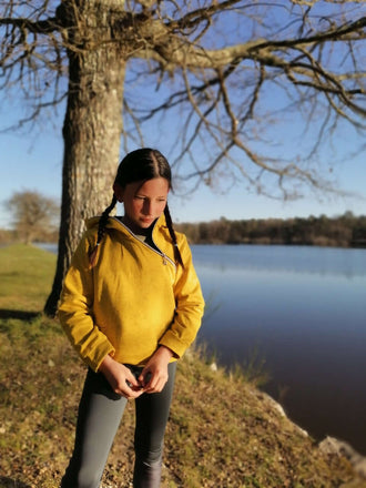 LE SWEAT ZIP ZAG 6- 16 ans porté par une jeune fille au bord d'un lac avec un pull jaune et des leggings.