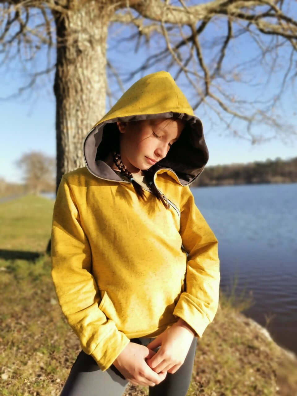 Le Sweat Zip Zag 6- 16 ans porté par une jeune fille au bord d'un lac, avec design original et capuche.