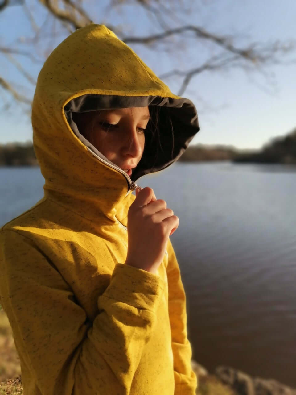 LE SWEAT ZIP ZAG 6- 16 ans porté près d'un lac avec une capuche unique et zip diagonal, idéal pour les jeunes.