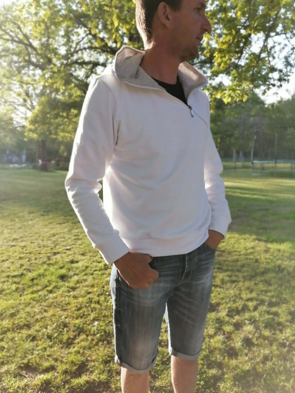 Homme portant LE SWEAT ZIP ZAG du XS au XXL en blanc avec un zip en diagonale dans un parc.