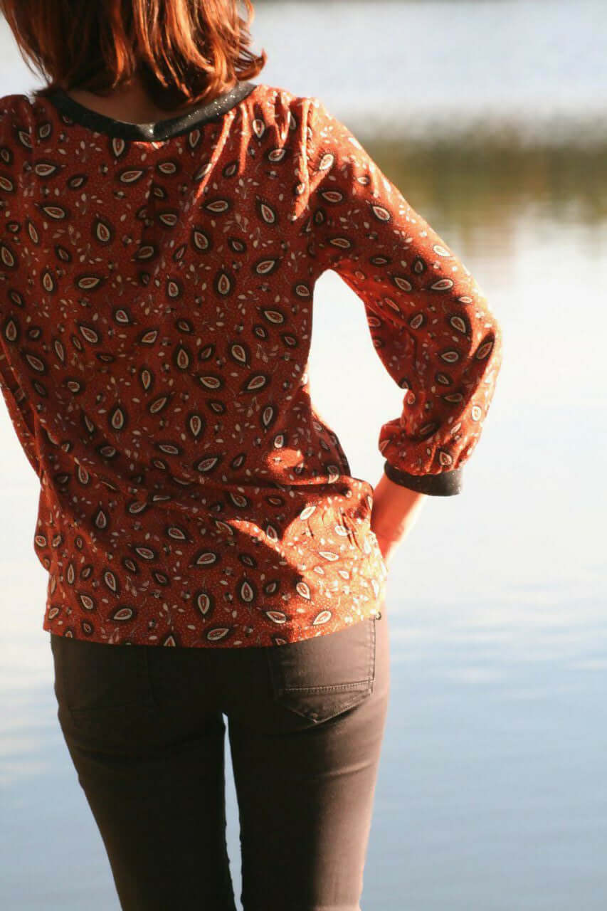 La Blouse CYCLADINE du 34 au 52 portée par une femme au bord de l'eau, mettant en valeur le tissu et le style sport-chic.