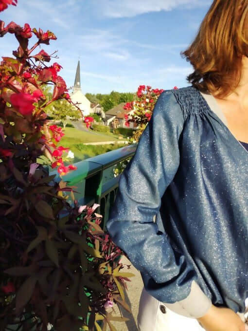 La veste BLOOMY du 34 au 46 portée avec des fleurs en arrière-plan, un look original et féminin.