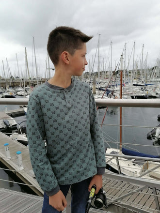 Un garçon portant le Polo ENJOY le Polo du 6 au 16 ans, devant un port avec des voiliers.