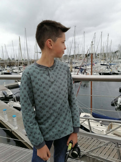 Un garçon portant le Polo ENJOY le Polo du 6 au 16 ans, devant un port avec des voiliers.