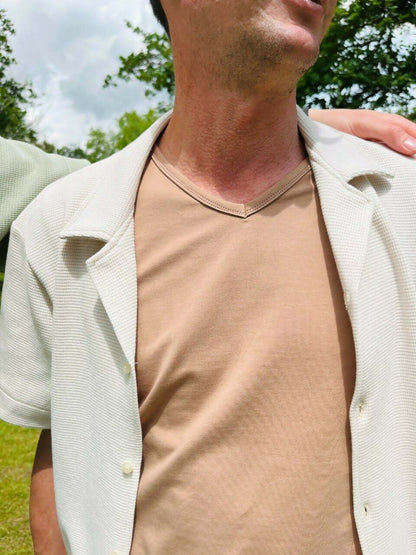 Le T-shirt Raoul du 38 au 54 porté par un homme avec un col V sous une chemise légère.