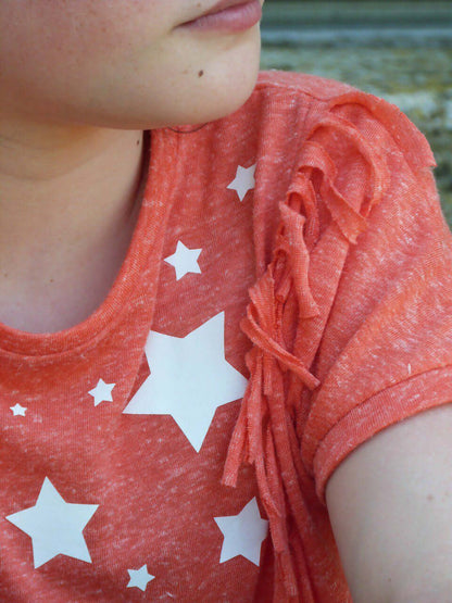 Le T-shirt et la Robe Rêve du 6 au 14 ans avec franges et étoiles sur fond orange.