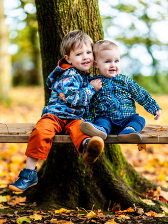 Deux enfants souriant portant des vestes colorées assis sur un banc en bois dans un cadre automnal