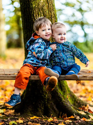 Deux enfants souriant portant des vestes colorées assis sur un banc en bois dans un cadre automnal