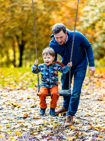 Homme poussant un enfant sur une balançoire en automne, avec des feuilles colorées au sol.