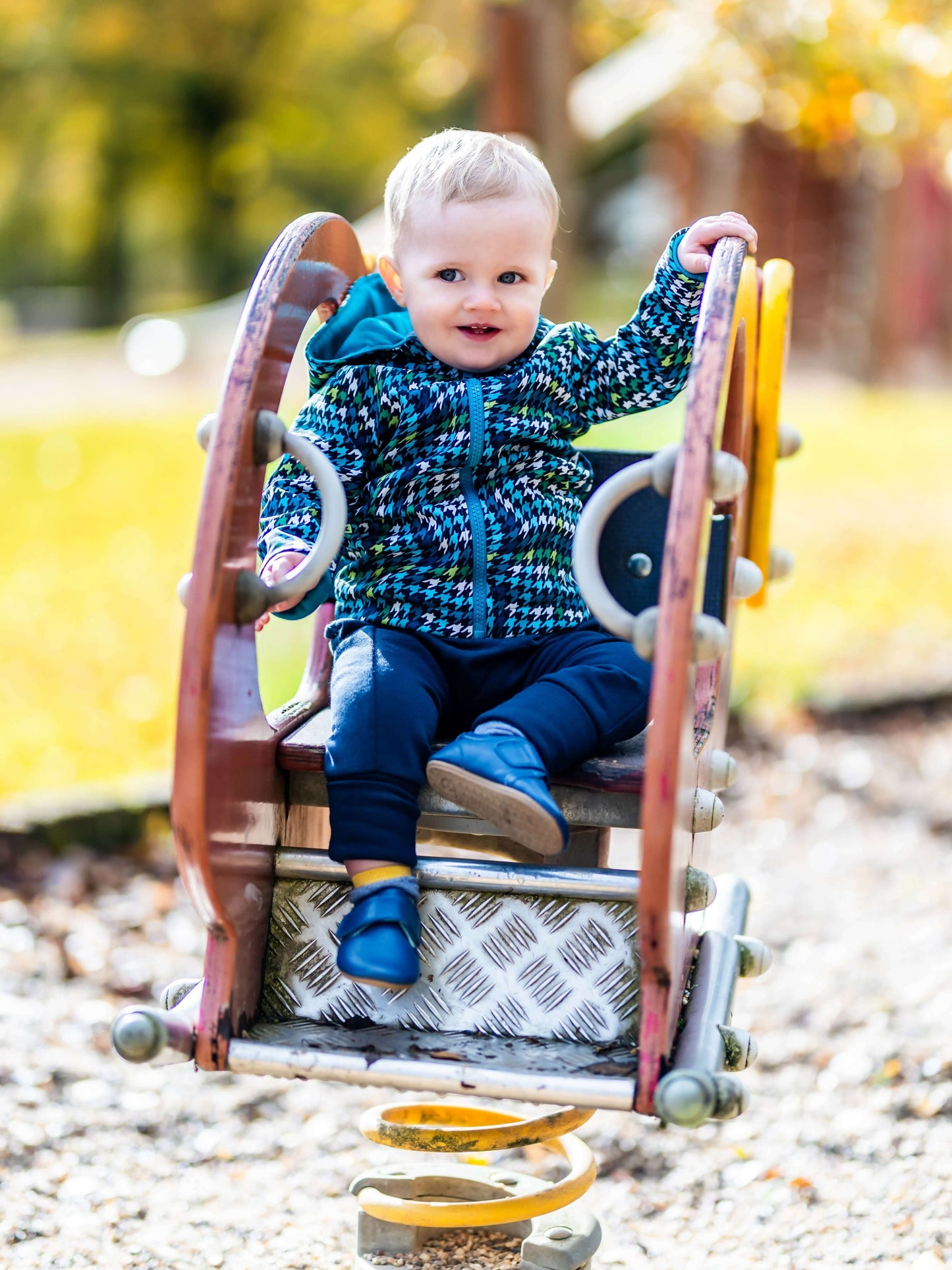 Un enfant en veste colorée joue sur une balançoire à ressort dans un parc en automne.