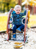 Un enfant en veste colorée joue sur une balançoire à ressort dans un parc en automne.