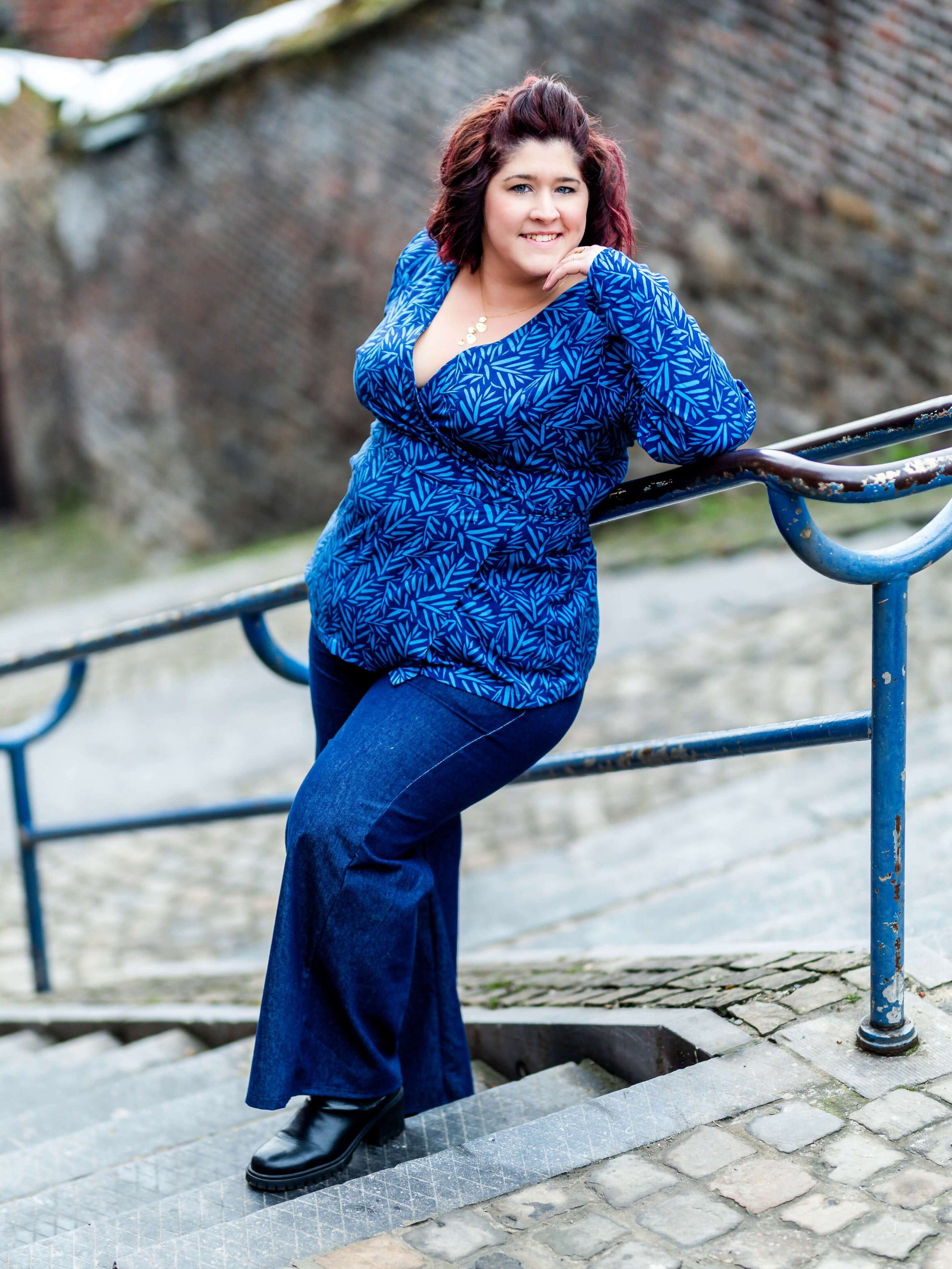 Femme portant MANDARINE : la robe / blouse portefeuille bleue, patron de couture pdf à télécharger, posant sur un escalier extérieur.