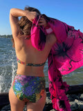 MELINA - Bikini pour femmes du 34 au 54, vue arrière sur la plage avec un maillot imprimé floral et un paréo rose, patron de couture PDF à télécharger.