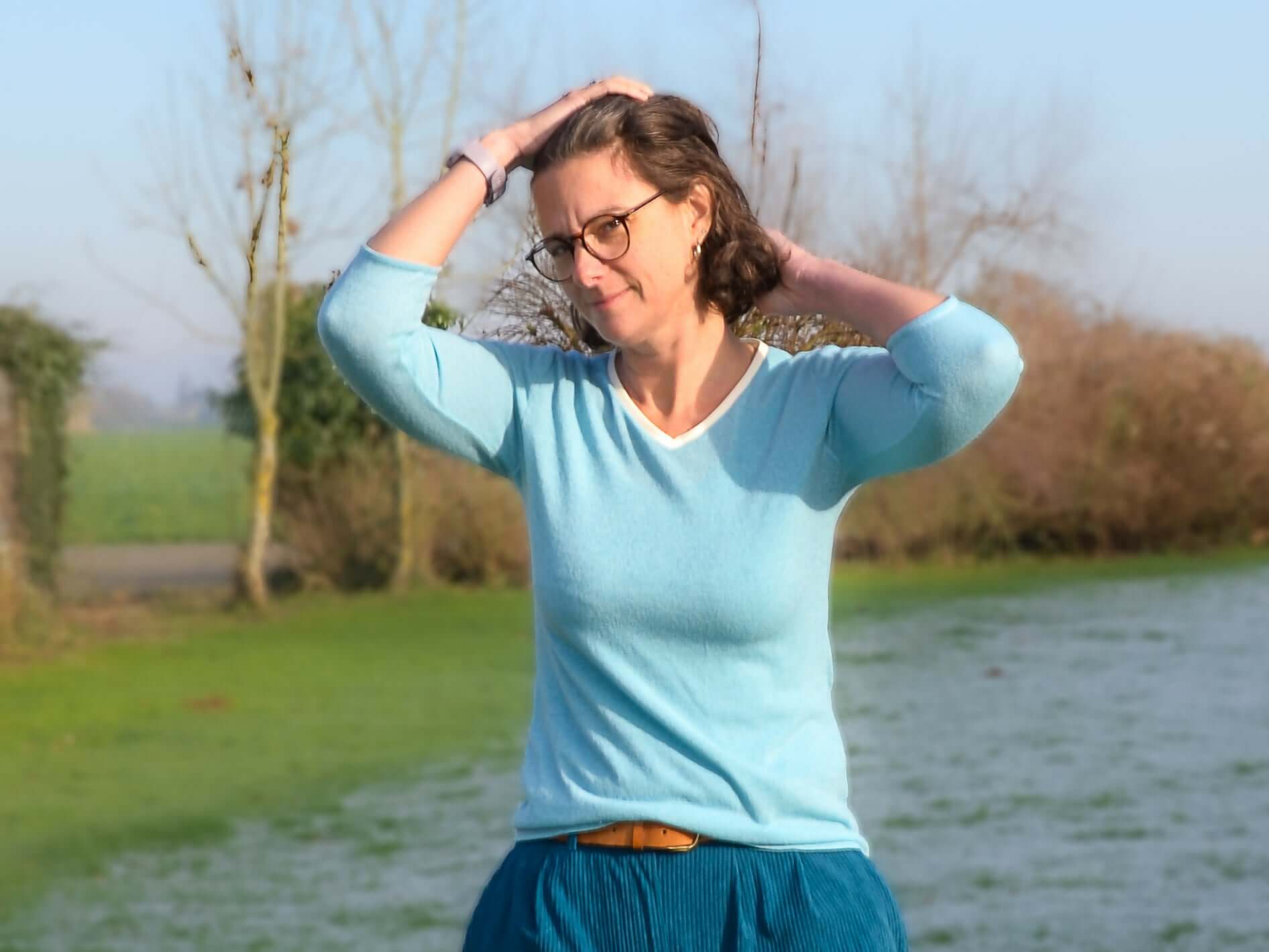Femme portant un pull bleu clair, manches longues, avec un col en V, posant en pleine nature.
