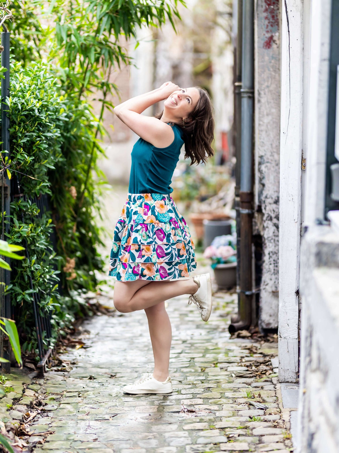 Femme portant MERISE - La jupette à volants, jupe colorée, sourire, patron de couture pdf à télécharger, dans une rue pavée lumineuse.