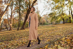 Femme portant un manteau beige en automne, forêt en arrière-plan