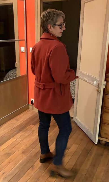 Personne portant le Manteau et Veste Jade rouge, patron de couture PDF à télécharger, vue de dos dans un intérieur chaleureux.