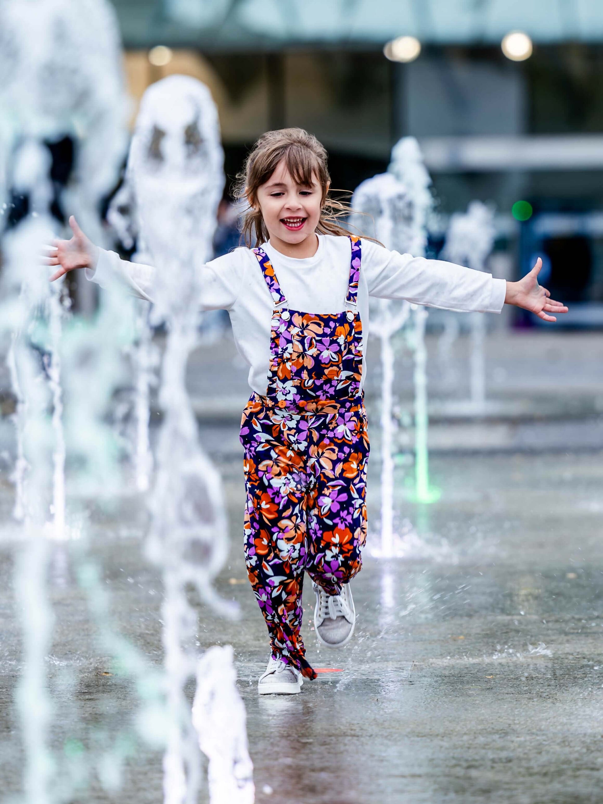 Enfant joyeux portant une salopette colorée en fleurs, jouant dans une fontaine en été.