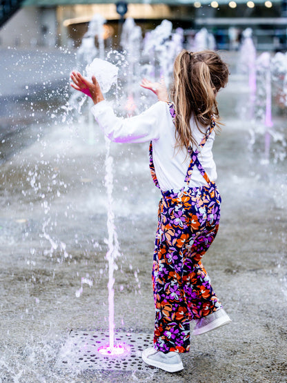 Petite fille en salopette colorée jouant dans une fontaine, parfaite pour un été joyeux avec du style.