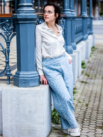 Femme portant un NASHI - Le pantalon palazzo bleu avec chemise blanche, patron de couture pdf à télécharger, appuyée contre un pilier.