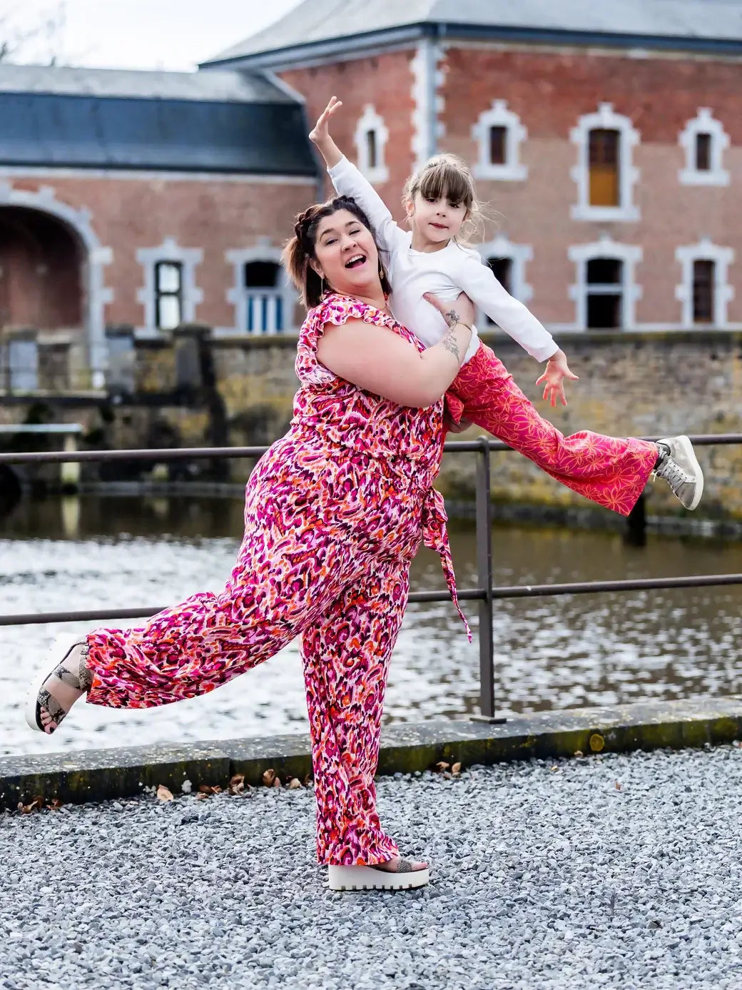 Femme et enfant posant joyeusement en vêtements colorés devant un bâtiment historique.