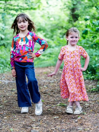 Deux enfants souriants portant des vêtements colorés posant dans un parc verdoyant, visage radieux.