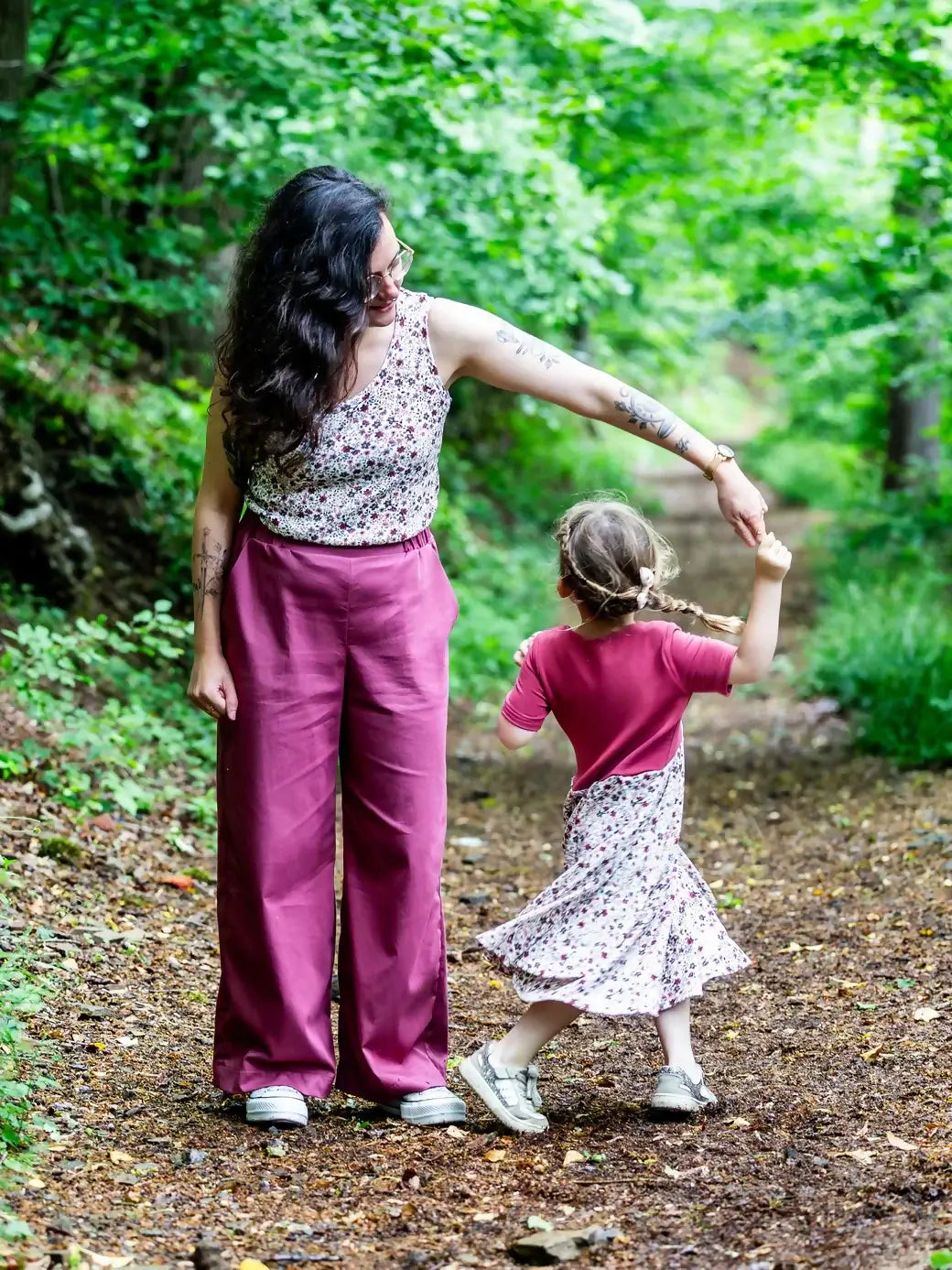 Mère et fille dansent dans la forêt, vêtues de vêtements floraux assortis, profitant d'un moment de complicité en nature.